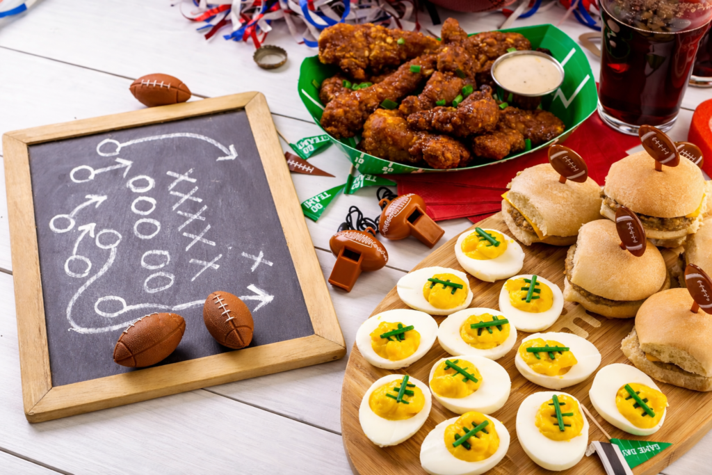 Football game day food spread with wings, sliders, deviled eggs, and a chalkboard football play diagram